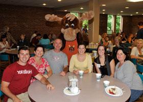 people sitting around a table in the cafeteria with a moose mascot