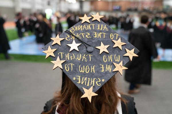 Graduate with a cap decorated with stars that reads All Thanks to the Stars Who Taught Me How To Shine
